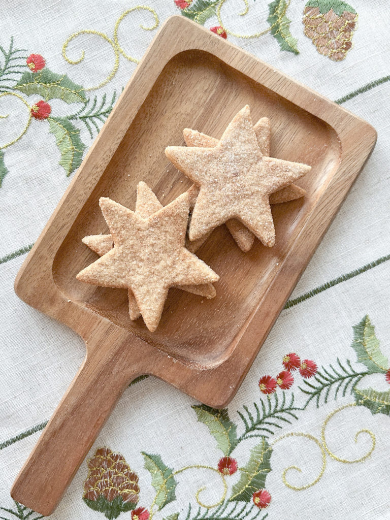 Tray of star-shaped Christmas cookies on holly-embroidered tablecloth