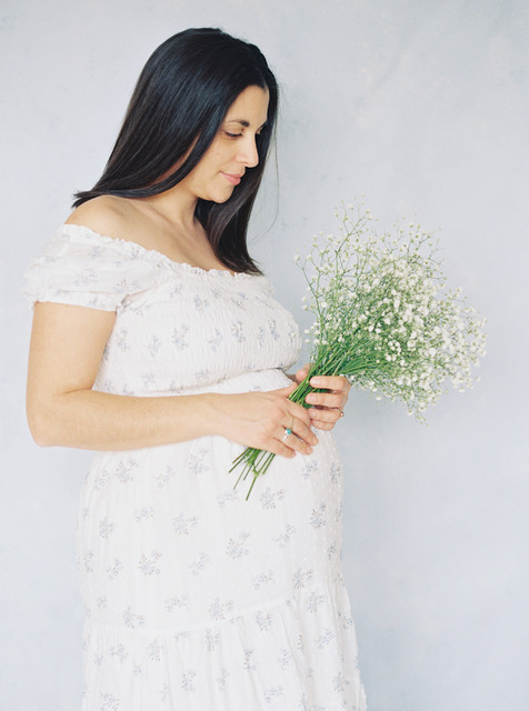 Pregnant woman in white dress holding a bouquet of baby's breath