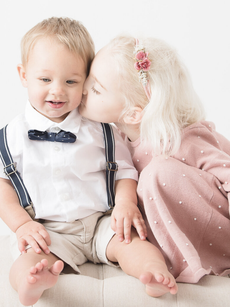 Little girl in pink dress kissing toddler brother 