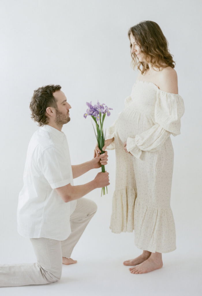 Man kneeling in front of pregnant woman and holding flowers out to her during maternity photoshoot